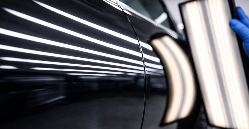 Close-up of straight reflection lines on a black vehicle door after professional dent removal.